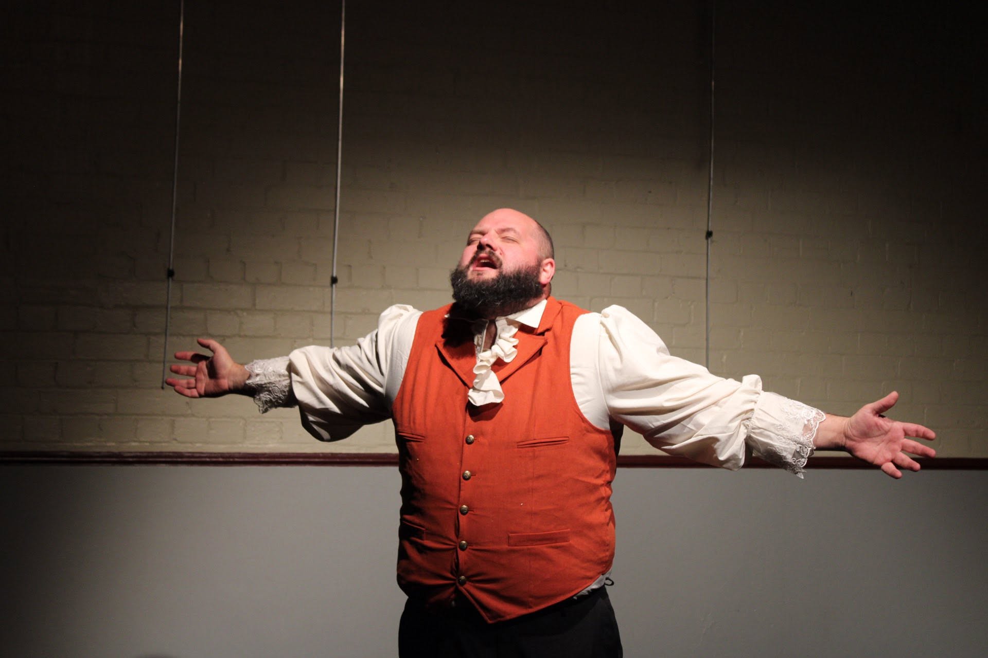 A performer with arms outstretched against the brick