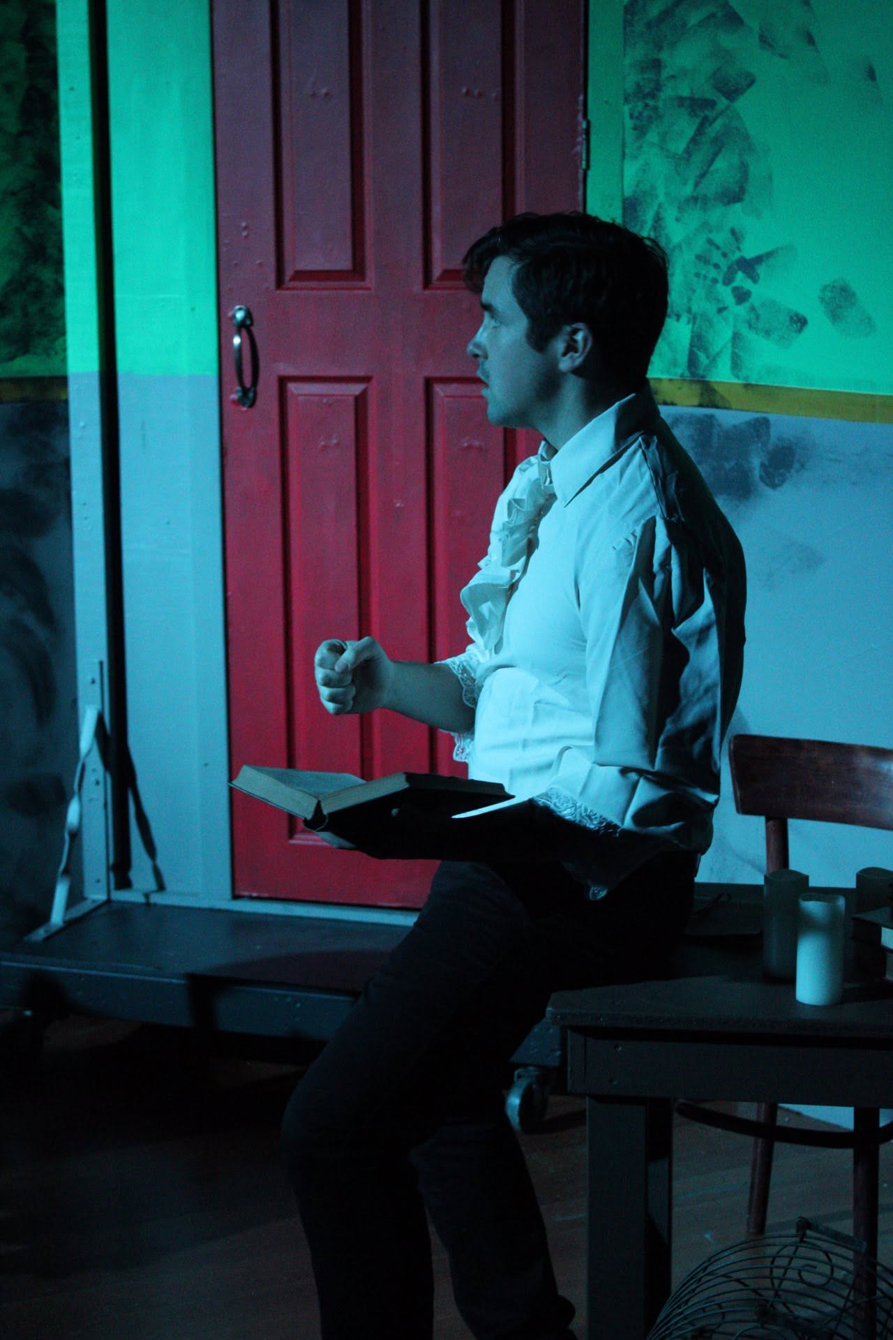 A performer reading from a book beside the red door